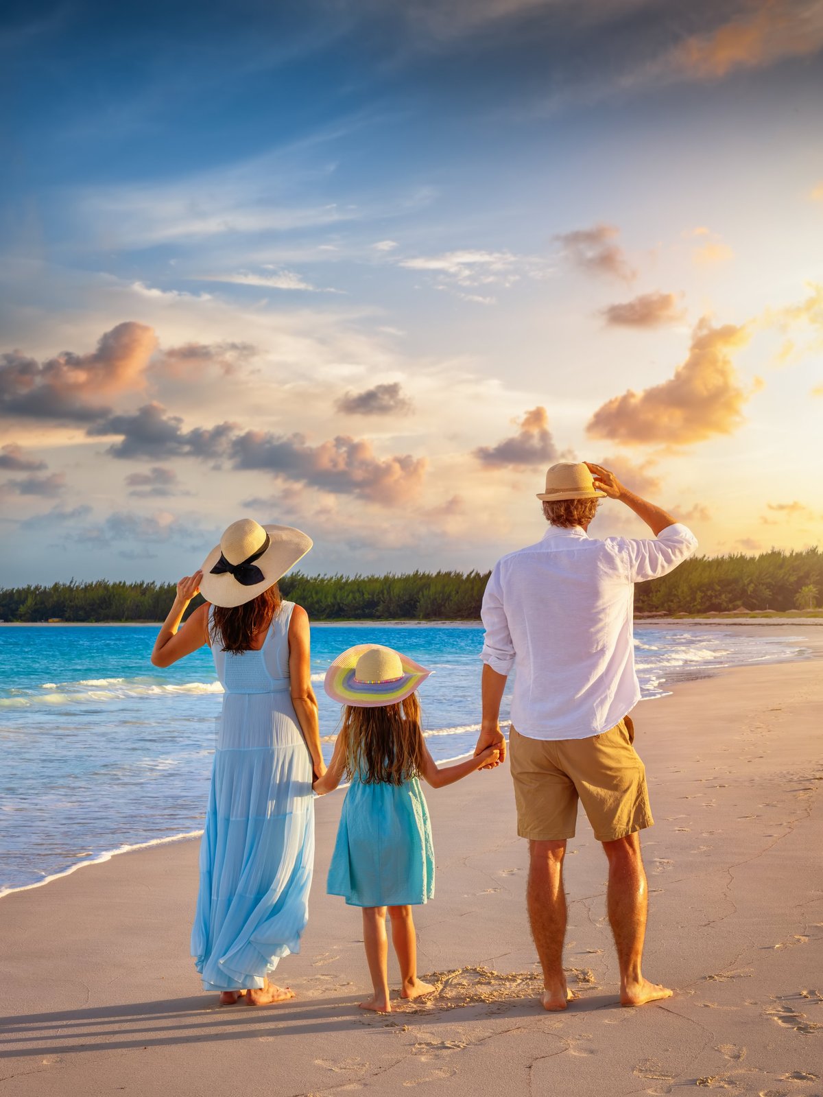 A family on summer holidays stands on a tropical beach during golden sunset time as a summer travel concept
