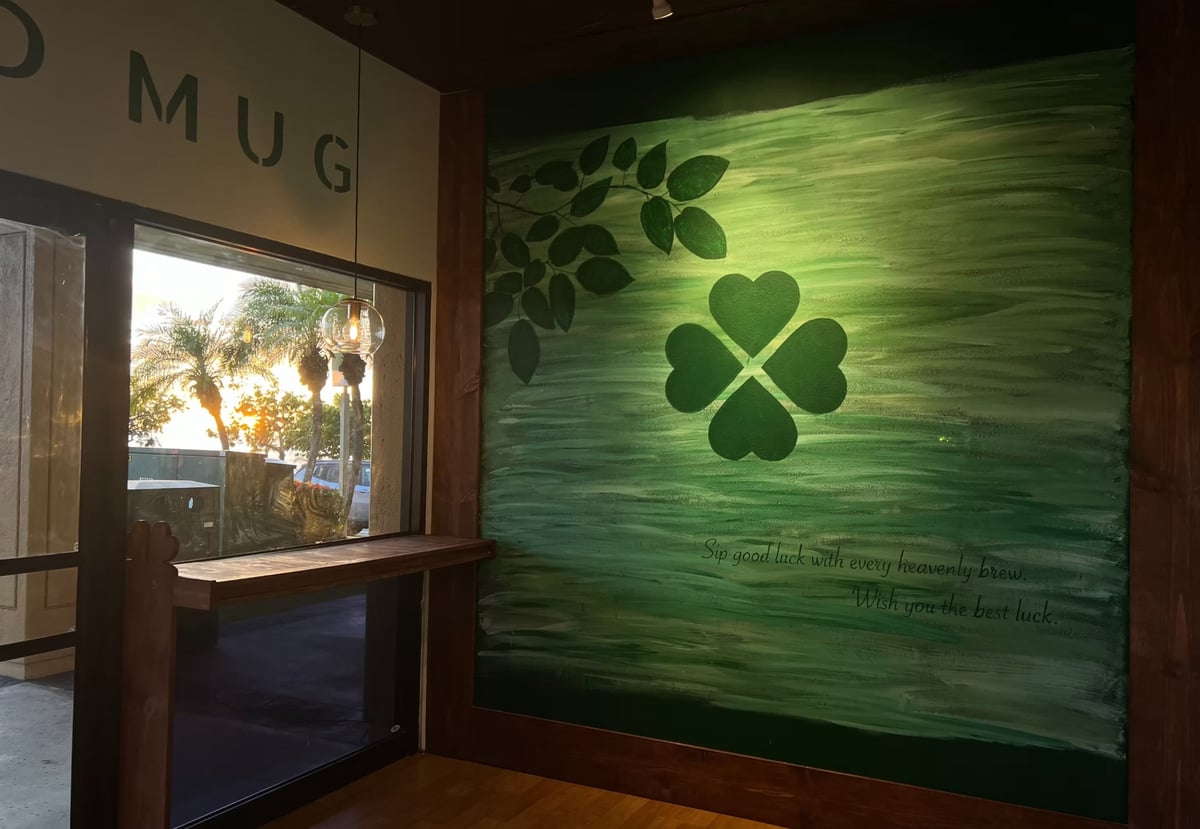 Green neon clover sign with leaf design on wooden wall inside modern storefront with MUG signage visible
