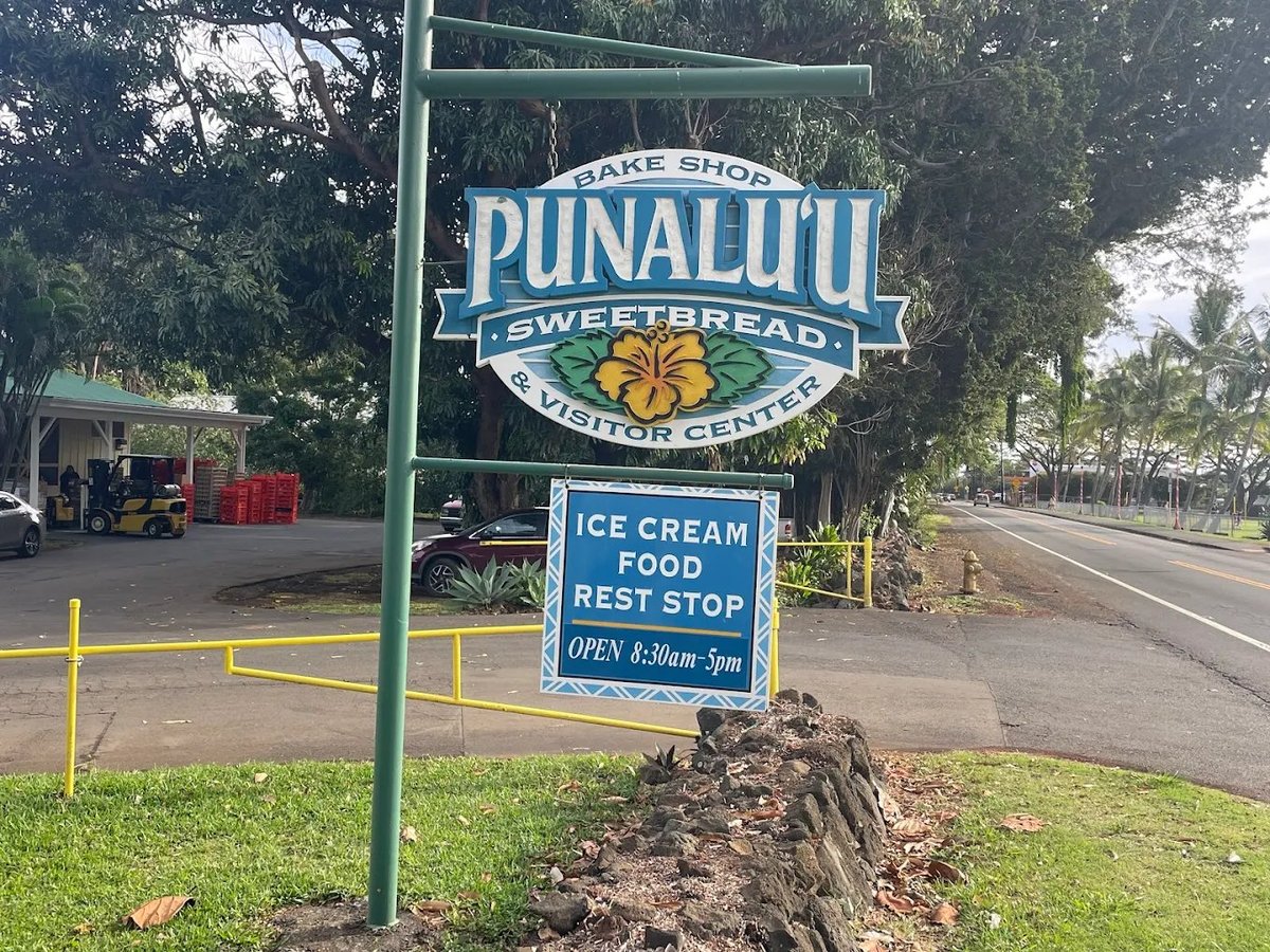Punaluuu Sweetbread shop sign advertising ice cream, food, and rest stop along a rural Hawaiian road with trees in background — Punalu'u Bake Shop in Na'alehu