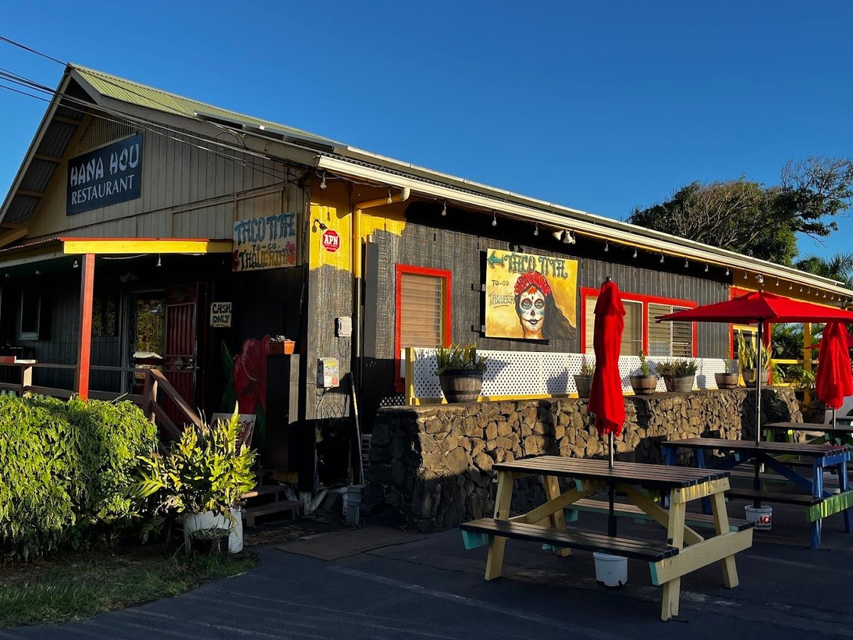Colorful roadside cafe or farm shop with yellow and red accents, wooden picnic tables, and decorative signage on a sunny day — Hana Hou in Na'alehu