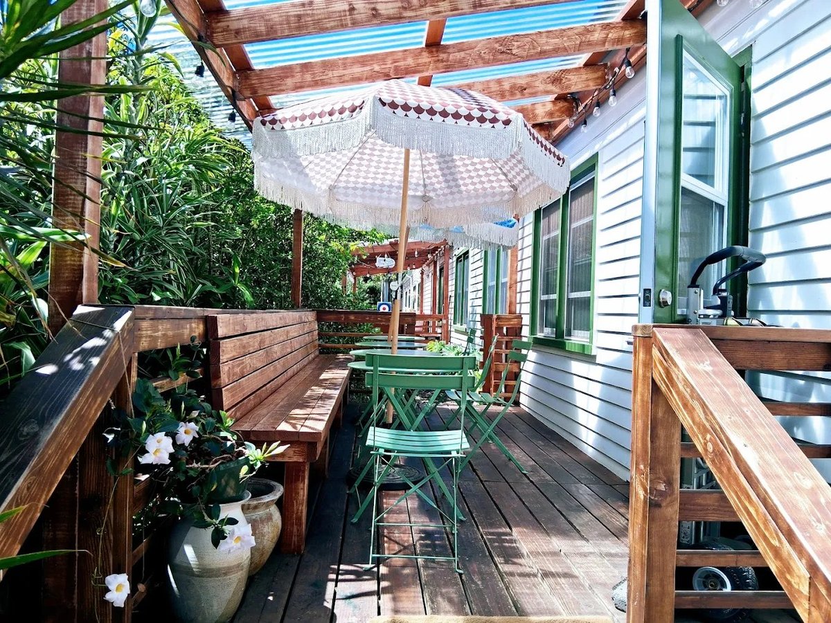 Wooden deck patio with white umbrella, potted plants, green chairs, and white house siding in background — Arvo Cafe in Kailua-Kona
